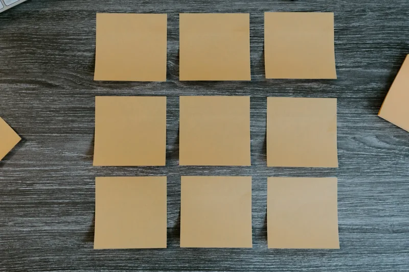 Nine blank yellow sticky notes on a wooden desk.